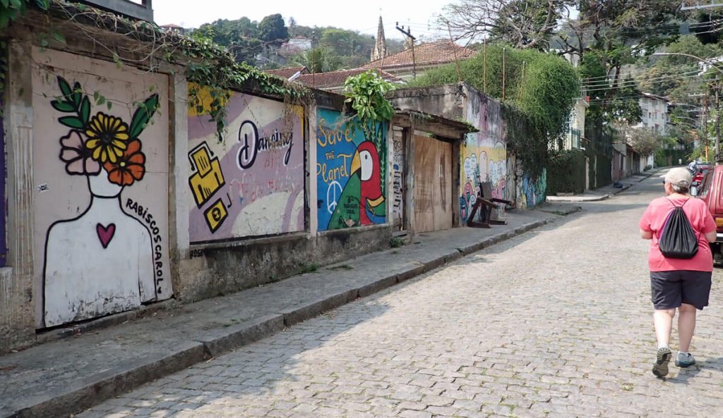 Sheila walks by mural on cobblestone street.