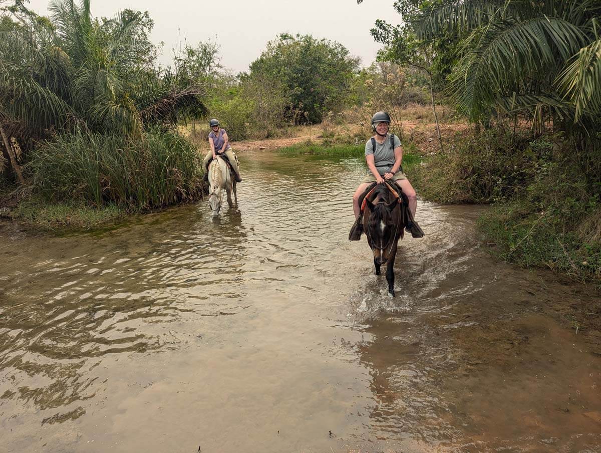 Sheila and Allison ride horses through water.